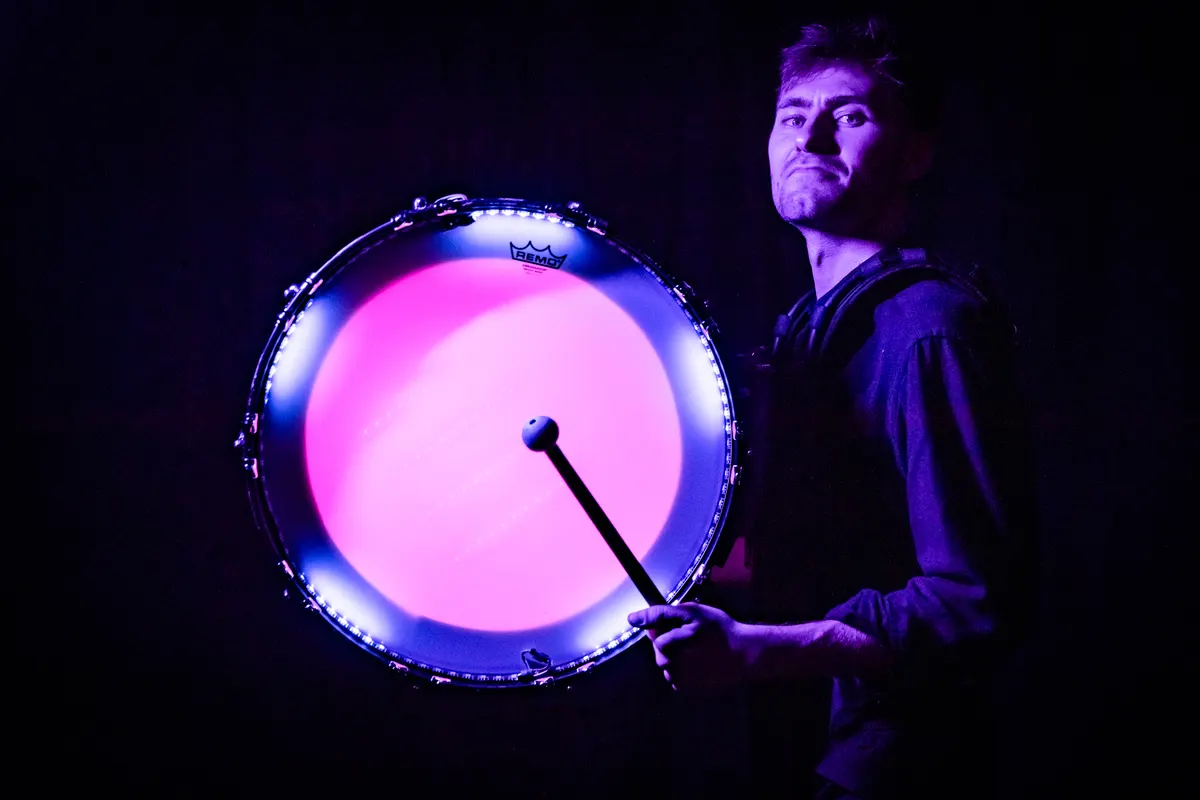 Drummer stands beside a bright pink LED-lit bass drum.